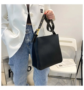 Detail view of large black leather bucket bag with wide strap and gold metal buckle