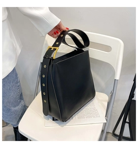 Detail of black bucket bag with wide leather strap featuring gold grommets and buckle