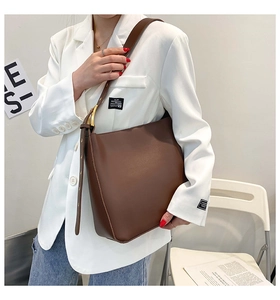 Detail of coffee brown leather bucket bag with gold buckle on a white blazer outfit