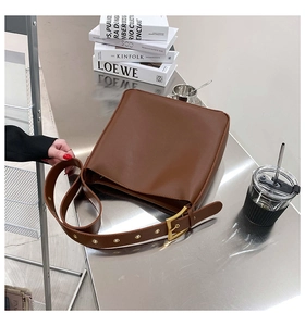 Detail of dark brown leather bag featuring wide strap with gold eyelets and buckle