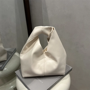 Minimalist cream dumpling cloud bag with knotted handle displayed on a stack of books