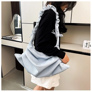 Detail of light blue pleated shoulder bag with decorative ruffles and bow on strap