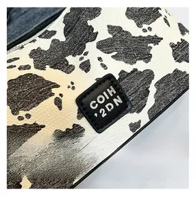 Close-up of cow print texture on leather handbag with COIH '2DN brand logo patch