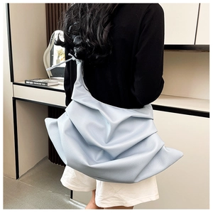 Detail of light blue pleated hobo bag with knotted strap on model in cozy interior setting