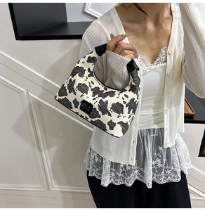 Detail of cow print hobo bag featuring black leather logo plaque and curved handle