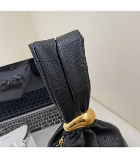 Detail of black pebbled leather handbag with gold metal ring and pleated handle design