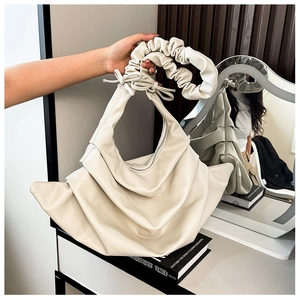 Detail of creamy white ruched handbag featuring lychee texture leather and bow handle