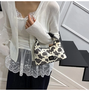 Close-up of small cow print underarm bag with black leather logo on a model side-wearing