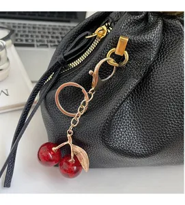 Detail of red cherry resin bag charm with gold alloy chain on black leather handbag