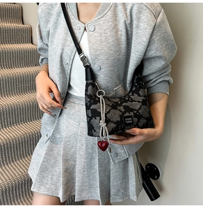 Detail of half-moon shoulder bag with abstract texture and red heart pendant accessory