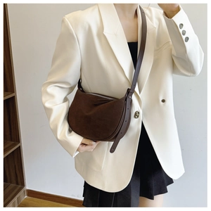 Brown suede half-moon crossbody bag shown on model wearing white suit and black skirt