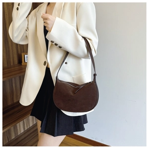 Detail of dark coffee suede crescent bag with zipper and thin strap worn with white blazer