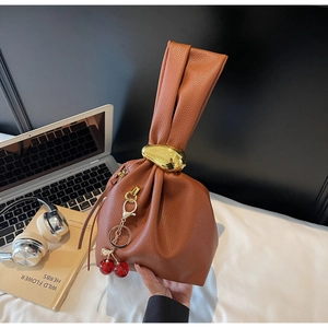 Brown lychee leather handbag with golden oval handle and cherry charm in a lifestyle setting