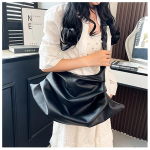 Detailed view of black pebbled leather crossbody bag with pleated texture and wide strap