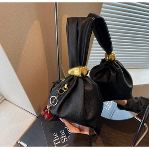 Detail of black pleated leather handbag with golden teardrop metal and cherry charm