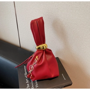 Detail of red pebbled leather handbag with pleated design and cherry charm accessory