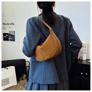 Close-up of caramel suede crescent shoulder bag styled on a model in a minimal setting