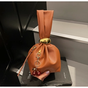 Close-up of brown pebble leather handbag with knotted handle and gold metal ring detail