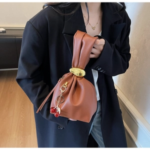 Detail of caramel pleated leather bag with gold ring handle and cherry charm on black blazer