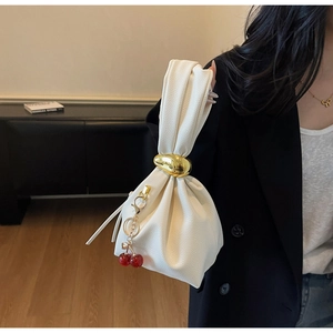 Detailed shot of white pleated handbag with gold hardware and a cherry charm