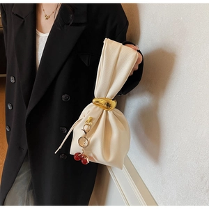 Detail of off-white lychee leather handbag featuring gold metal rings and a cherry charm
