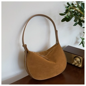 Detail of caramel suede half-moon bag featuring smooth leather strap and retro silhouette