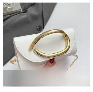 Detail of white clutch with C-shaped gold handle and removable thin metal chain strap