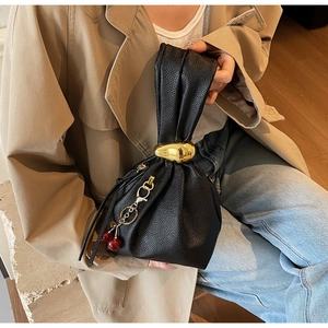 Detail of black lychee grain leather bucket bag with gold ball hardware and cherry charm