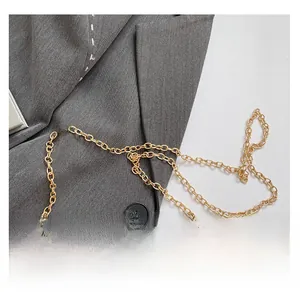 Close-up of a glossy gold metal chain strap on a blazer, showing flat oval links