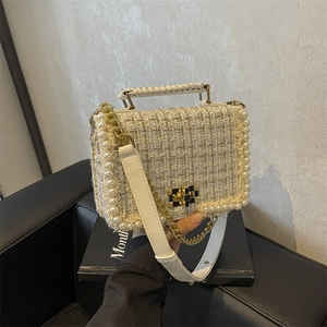 Beige tweed handbag with pearl trim and gold chain strap shown being held by a model