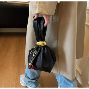 Close-up of black pleated leather handbag with gold ring and cherry charm detail