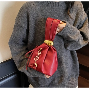 Close-up of red lychee leather handbag with golden ring handle and cherry charm detail
