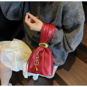Detail of red lychee grain leather handbag with gold ball buckle and cherry pendant