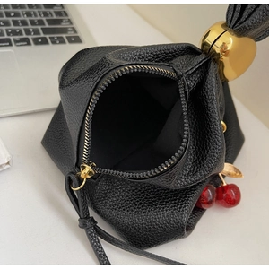Detail of black pebbled leather handbag featuring a gold heart handle and cherry charm