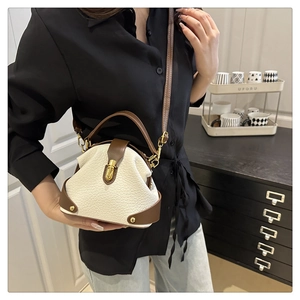 Close-up of cream textured leather handbag with brown trim and gold clasp on a shelf