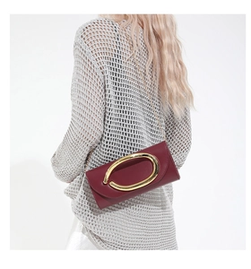 Model wearing a wine red crossbody bag with a large gold buckle and slim chain strap