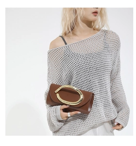 Detail of a brown leather clutch featuring a large golden C-shaped metallic buckle and flap