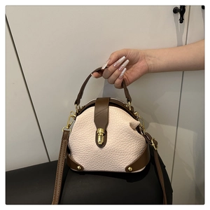 Detail of cream leather crossbody bag with brown trim and golden turn-lock closure