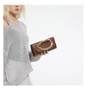 Brown leather handbag detail featuring a large gold U-shaped metal buckle and flap cover