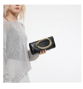 Detail of a black leather clutch featuring a prominent gold U-shaped metal handle