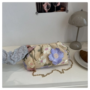 Détail des broderies florales et de la chaîne dorée sur le sac nuage en paille