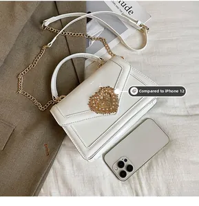White patent leather crossbody bag with pearl heart buckle shown next to phone for scale