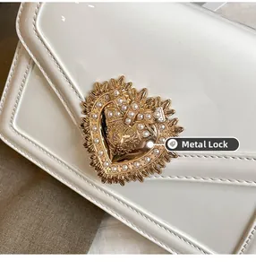 Detail of white patent leather bag featuring a gold heart clasp with pearls and bow