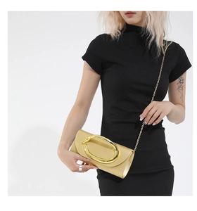 Detail of champagne gold clutch bag featuring oversized oval metallic buckle and gold chain