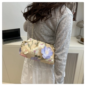 Détail de la broderie florale sur un sac nuage beige avec chaîne dorée porté par mannequin
