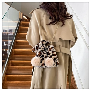 Detail of plush leopard print bucket bag with metal chain strap and decorative pom-poms