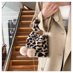 Detail of leopard print faux fur bucket bag with beige pom-poms and metal chain strap
