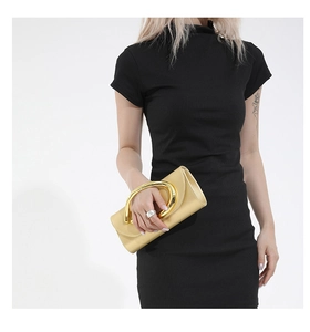 Detail of a shiny gold clutch bag with a chunky metal ring handle on black rib-knit dress