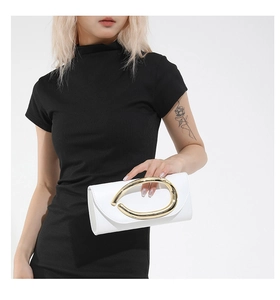 Detail of a white crossbody bag with a large oval gold metal handle on a black dress