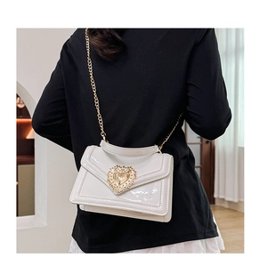 Detail of white patent leather shoulder bag with embossed gold heart buckle and chain strap